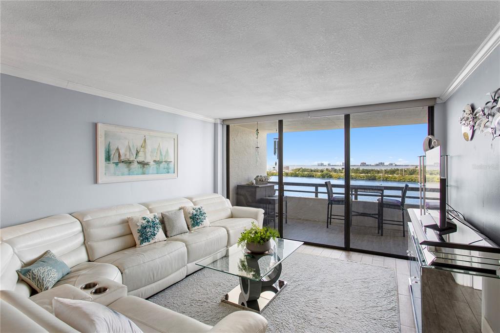 A living room with a white sectional sofa, glass coffee table, and a balcony overlooking water — 5701 MARINER STREET UNIT 504A, TAMPA, FL