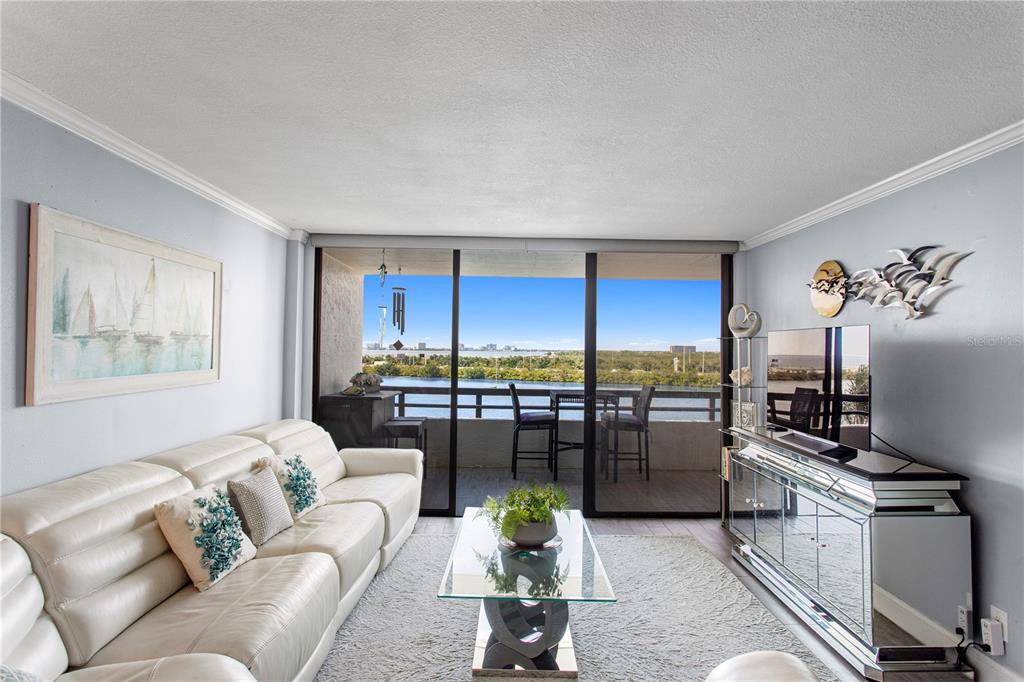 A living room with a white leather sofa, glass coffee table, and a balcony overlooking water — 5701 MARINER STREET UNIT 504A, TAMPA, FL