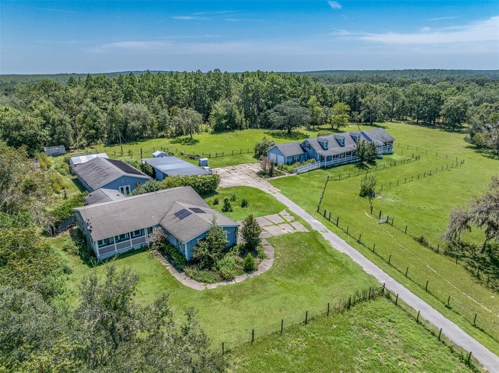 An aerial view shows two blue houses on a large, grassy, fenced-in rural property — 1474 W JACKSON HILL COURT, LECANTO, FL