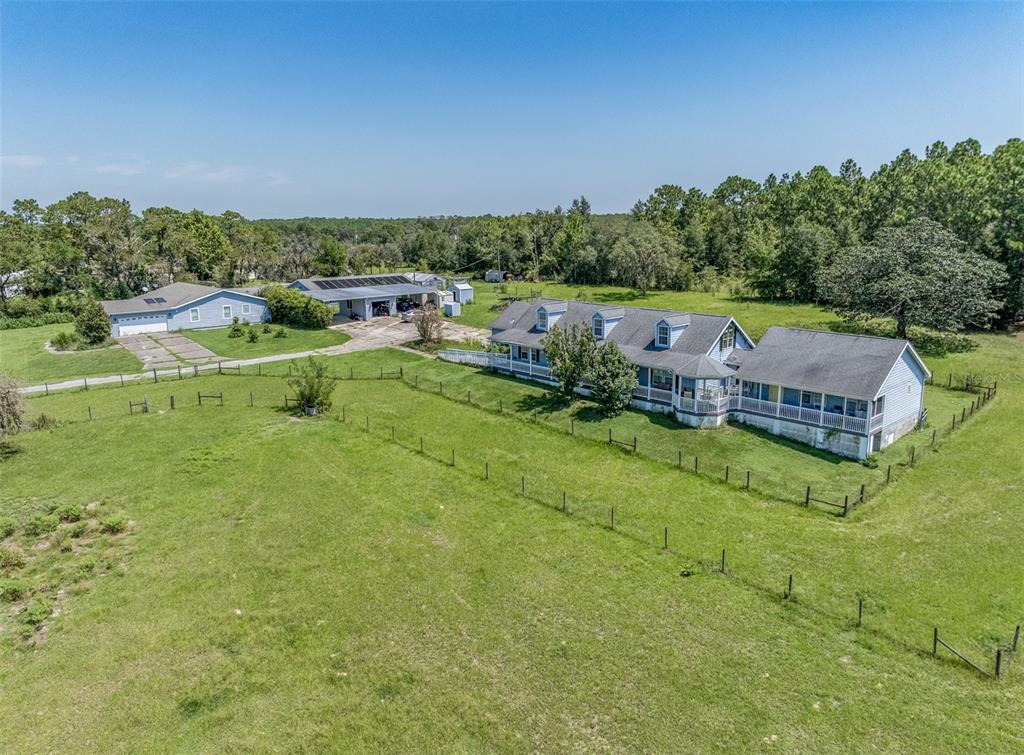 An aerial view shows a house with a wrap-around porch, a garage, and fenced pasture — 1474 W JACKSON HILL COURT, LECANTO, FL