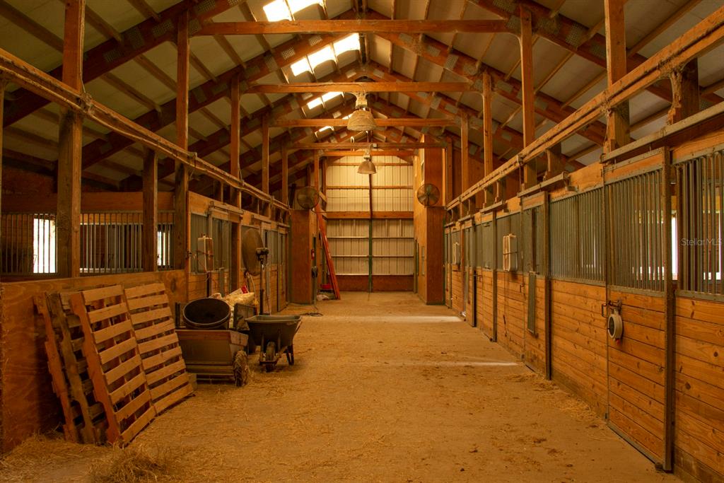 A rustic horse barn interior features wooden stalls, a dirt floor, and exposed ceiling rafters — 1474 W JACKSON HILL COURT, LECANTO, FL