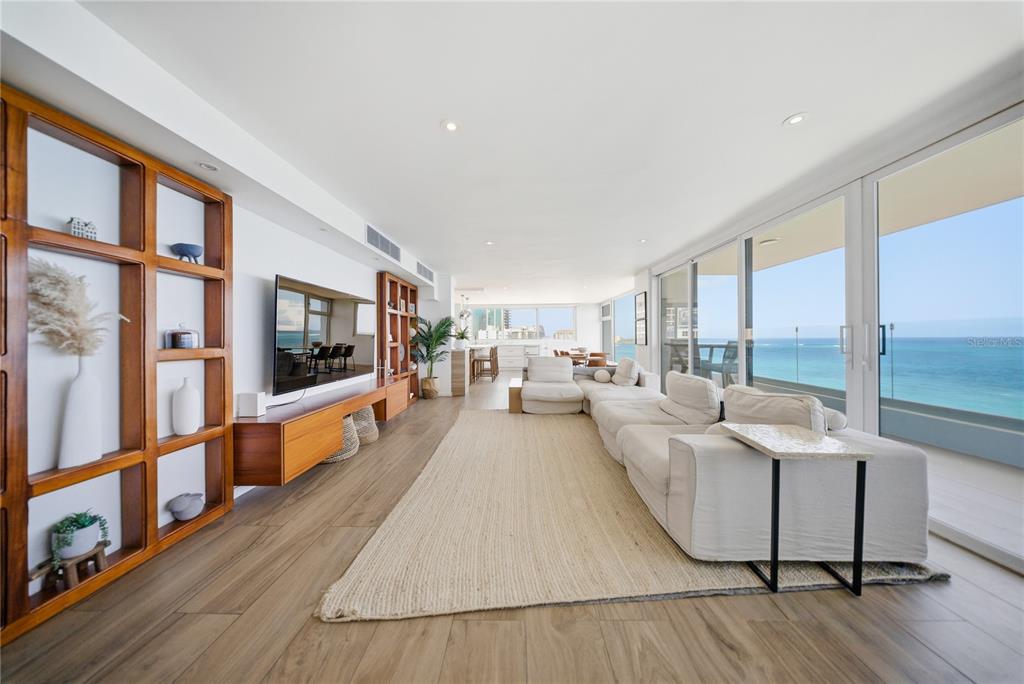 A modern living room features a large sectional sofa, wooden shelving, and floor-to-ceiling ocean views — 1 CERVANTES UNIT 9 PH, SAN JUAN, PR