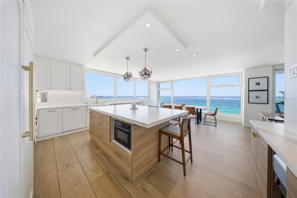 A modern kitchen with a wood-toned island, white cabinetry, and floor-to-ceiling windows overlooking the ocean — 1 CERVANTES UNIT 9 PH, SAN JUAN, PR