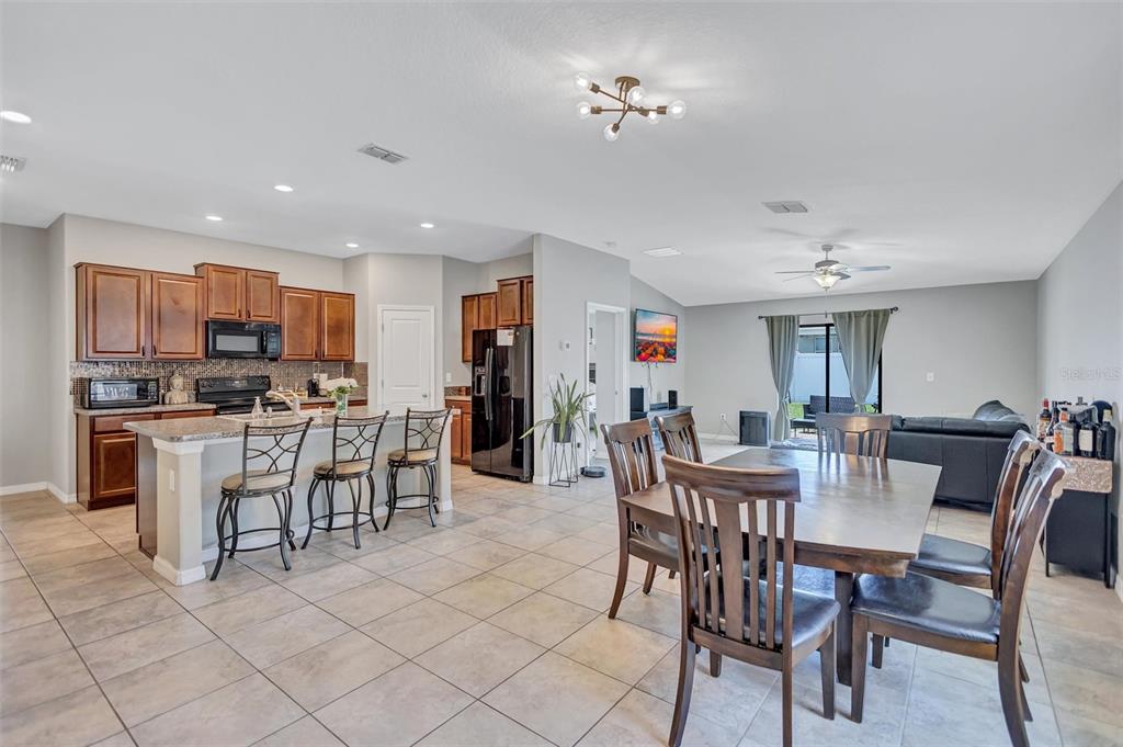 An open-concept kitchen and dining area featuring wooden cabinets, tile flooring, and a breakfast bar — 14106 COVERT GREEN PLACE, RIVERVIEW, FL