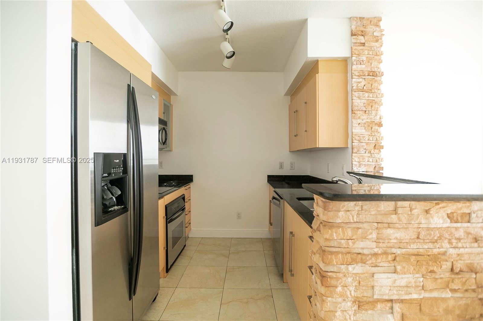 A galley kitchen features light wood cabinets, black countertops, stainless steel appliances, and stone accents — 335 S Biscayne Blvd # 2710, Miami FL 33131, MIAMI, FL