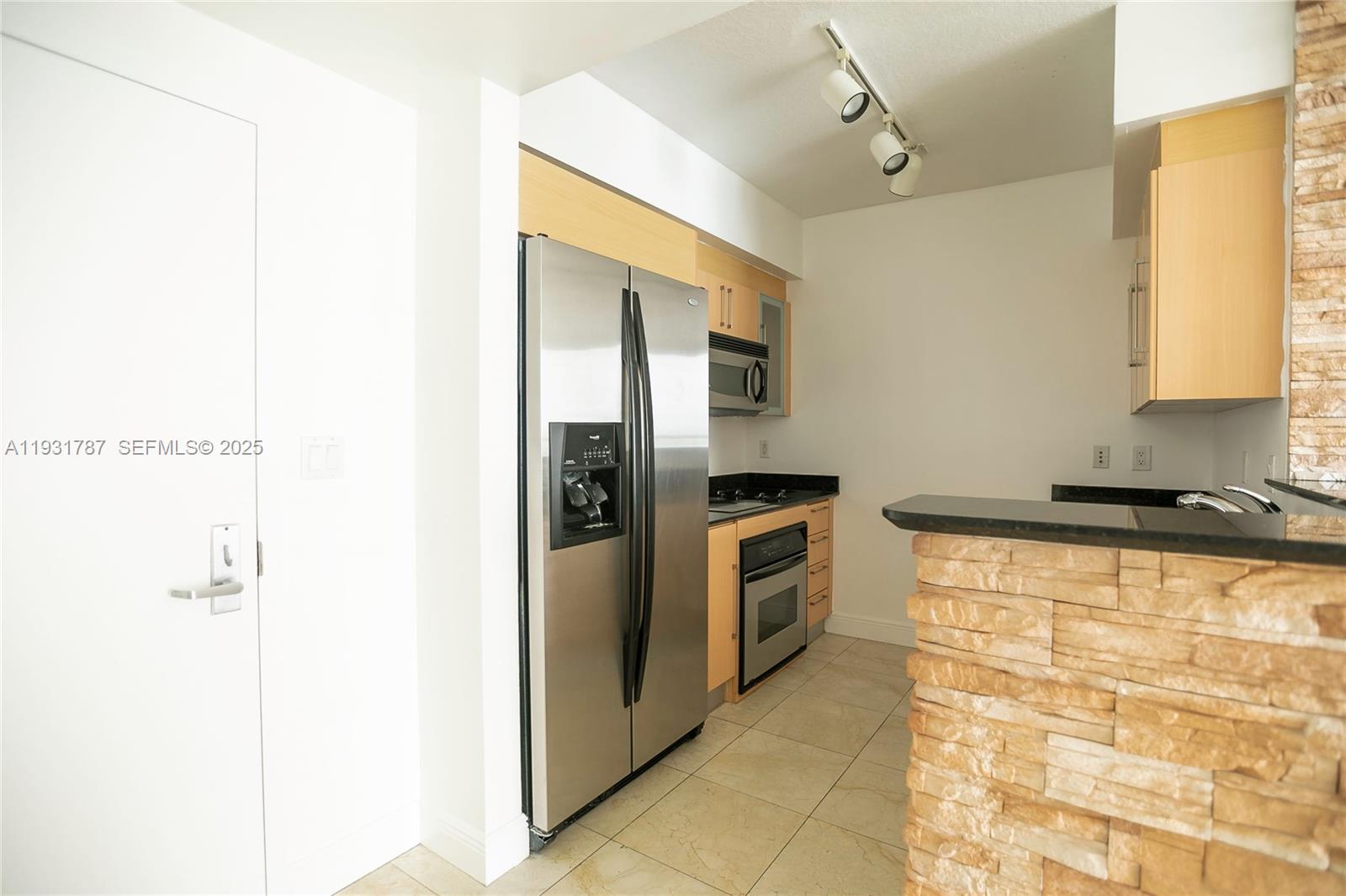 A kitchen features stainless steel appliances, light wood cabinets, and a stone-faced breakfast bar — 335 S Biscayne Blvd # 2710, Miami FL 33131, MIAMI, FL