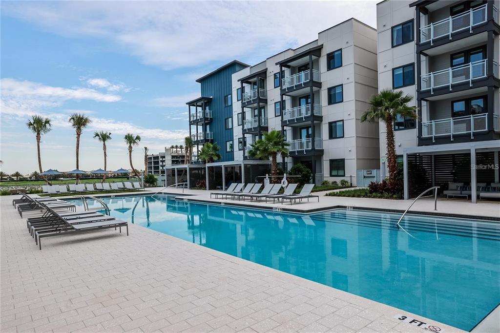 A swimming pool with lounge chairs sits in front of a modern multi-story apartment building — 5127 W TYSON AVENUE UNIT A2 den, TAMPA, FL