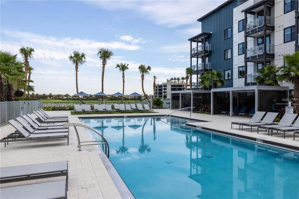 A swimming pool with lounge chairs on a paved deck beside a modern apartment building — 5127 W TYSON AVENUE UNIT A2 den, TAMPA, FL