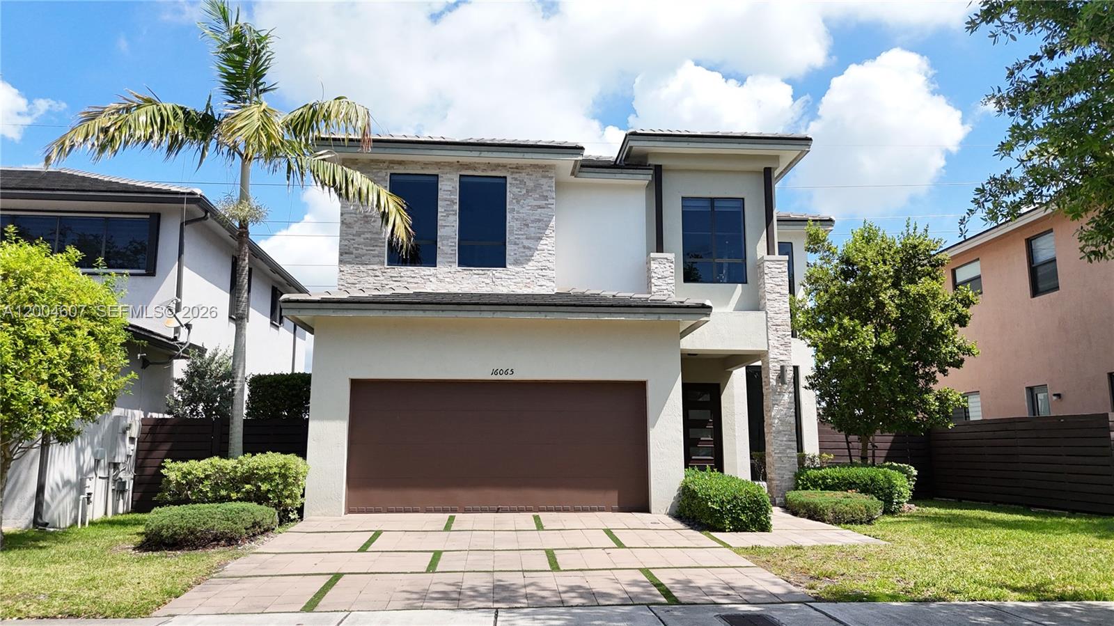 A two-story house features a brown garage door, stone accents, and a paved driveway — 16065 SW 136th Ter, Miami FL 33196, MIAMI, FL