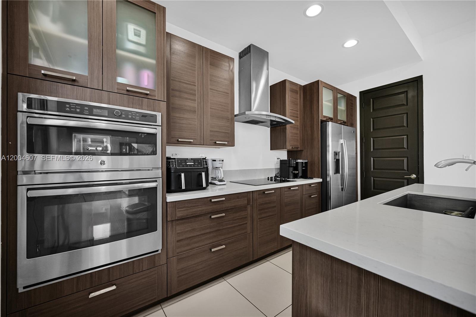 A modern kitchen features dark wood cabinetry, stainless steel appliances, and white quartz countertops — 16065 SW 136th Ter, Miami FL 33196, MIAMI, FL