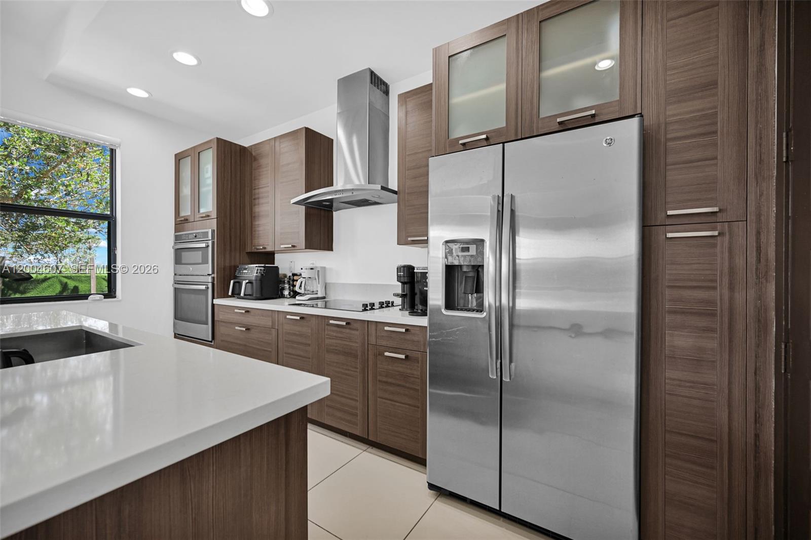 A modern kitchen features wood-grain cabinets, stainless steel appliances, and a white quartz island — 16065 SW 136th Ter, Miami FL 33196, MIAMI, FL