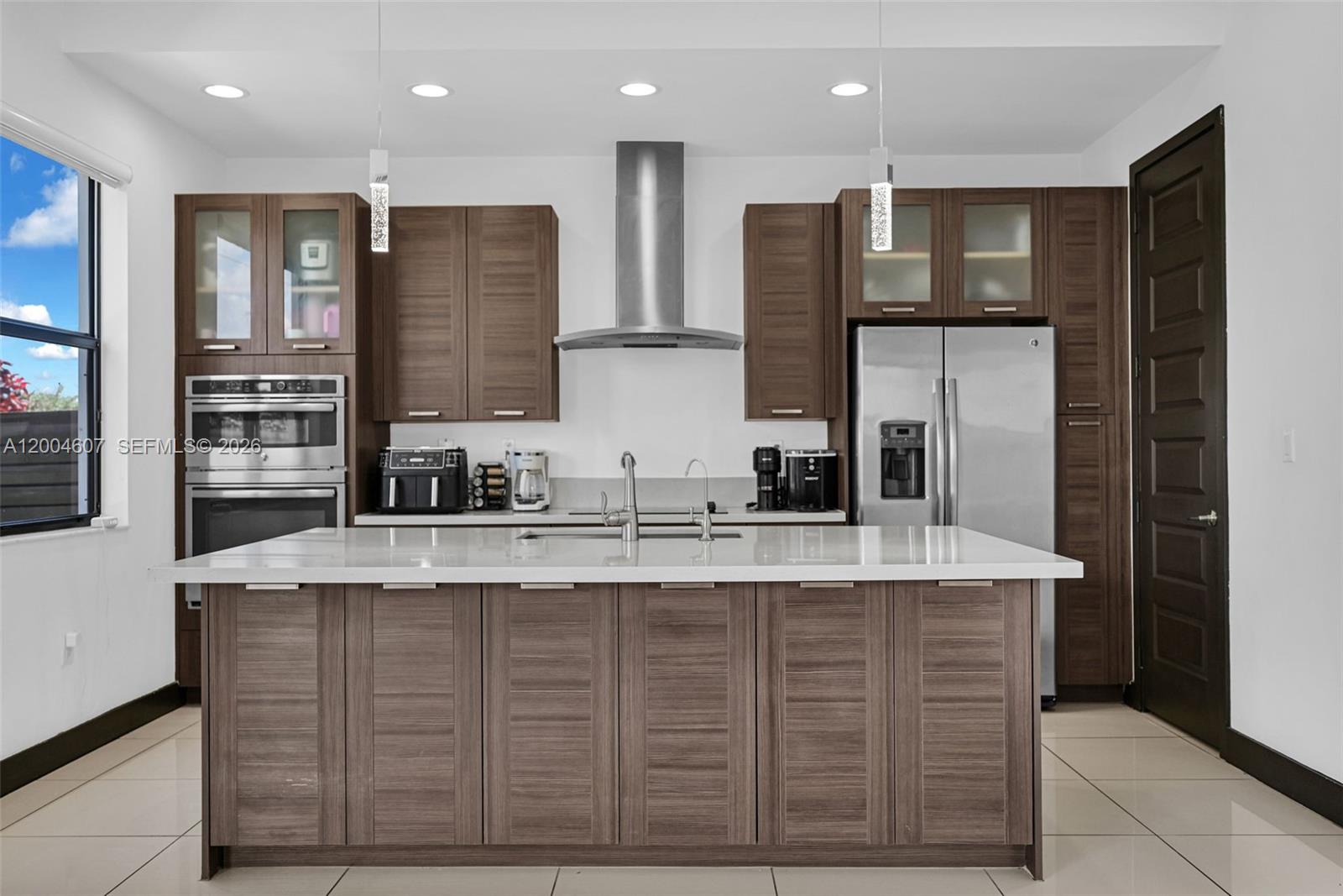 A modern kitchen features wood-grain cabinets, a large white island, and stainless steel appliances — 16065 SW 136th Ter, Miami FL 33196, MIAMI, FL