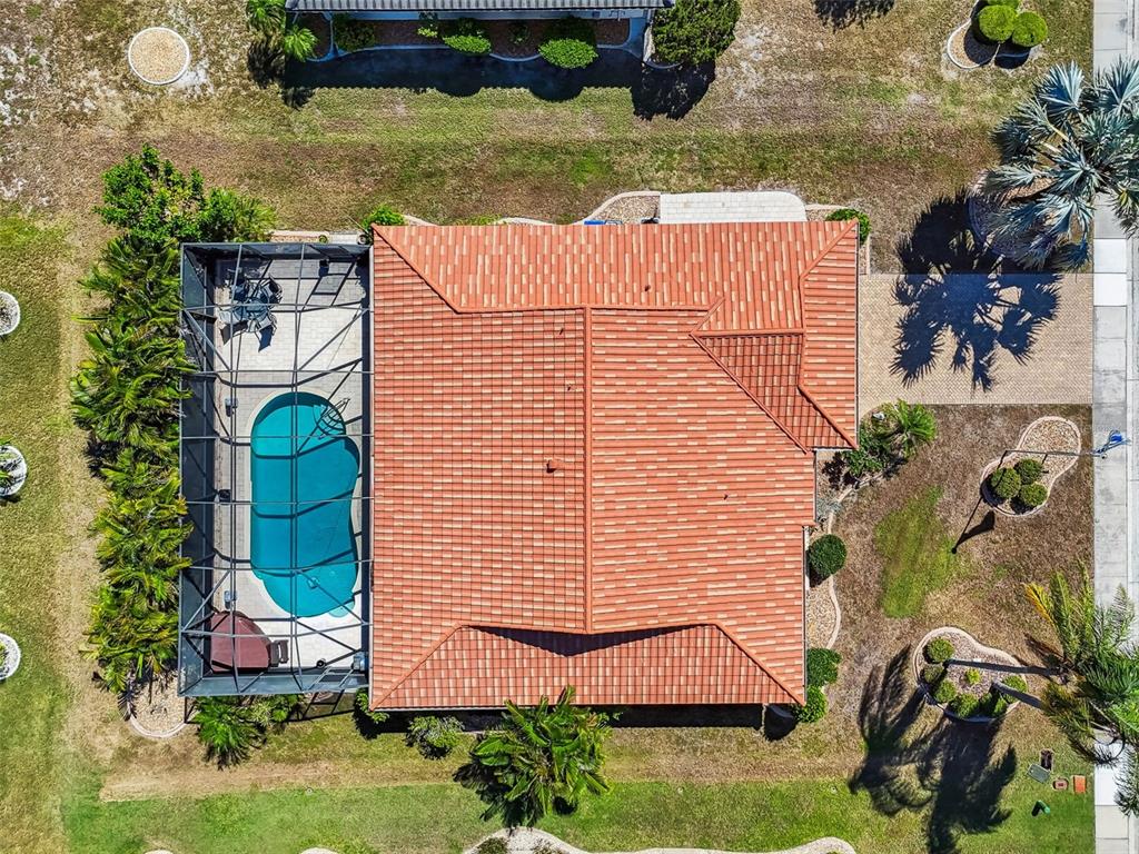 An aerial view shows a house with a red tile roof and a screened-in pool — 706 PLUMBROOK ROAD, SUN CITY CENTER, FL