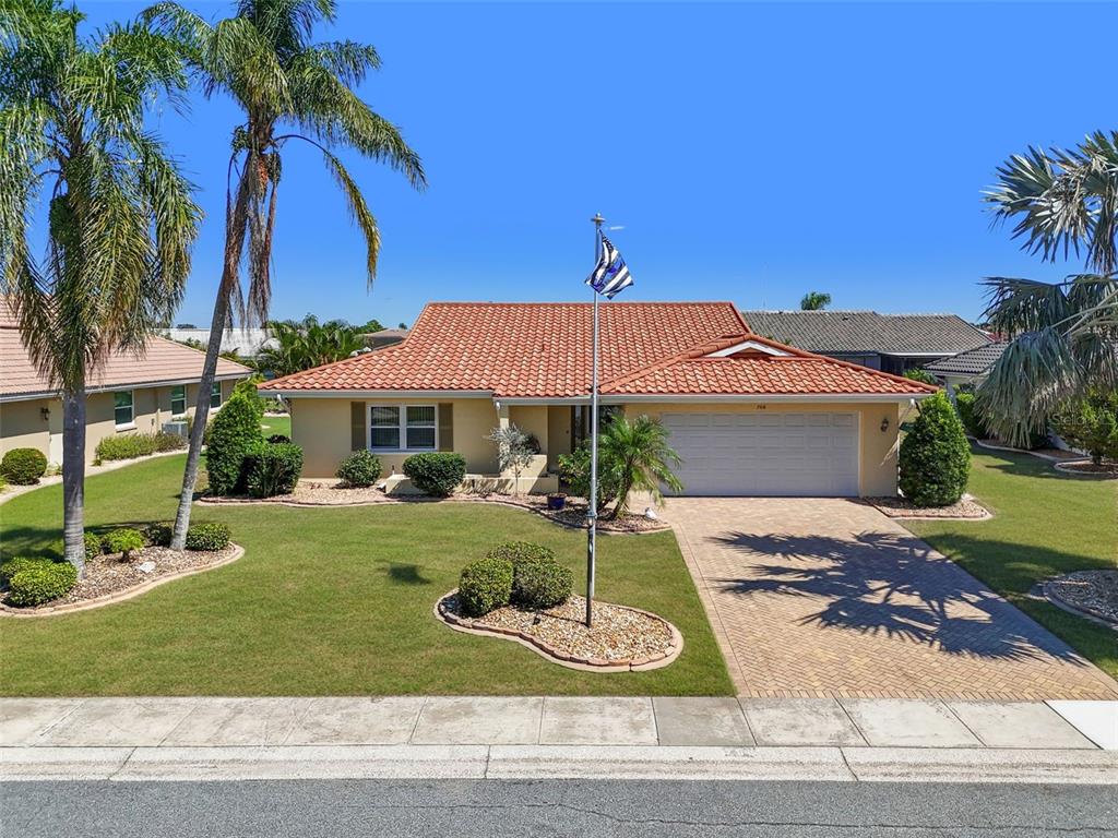 A single-story house with a red tile roof, a paved driveway, and a flagpole — 706 PLUMBROOK ROAD, SUN CITY CENTER, FL