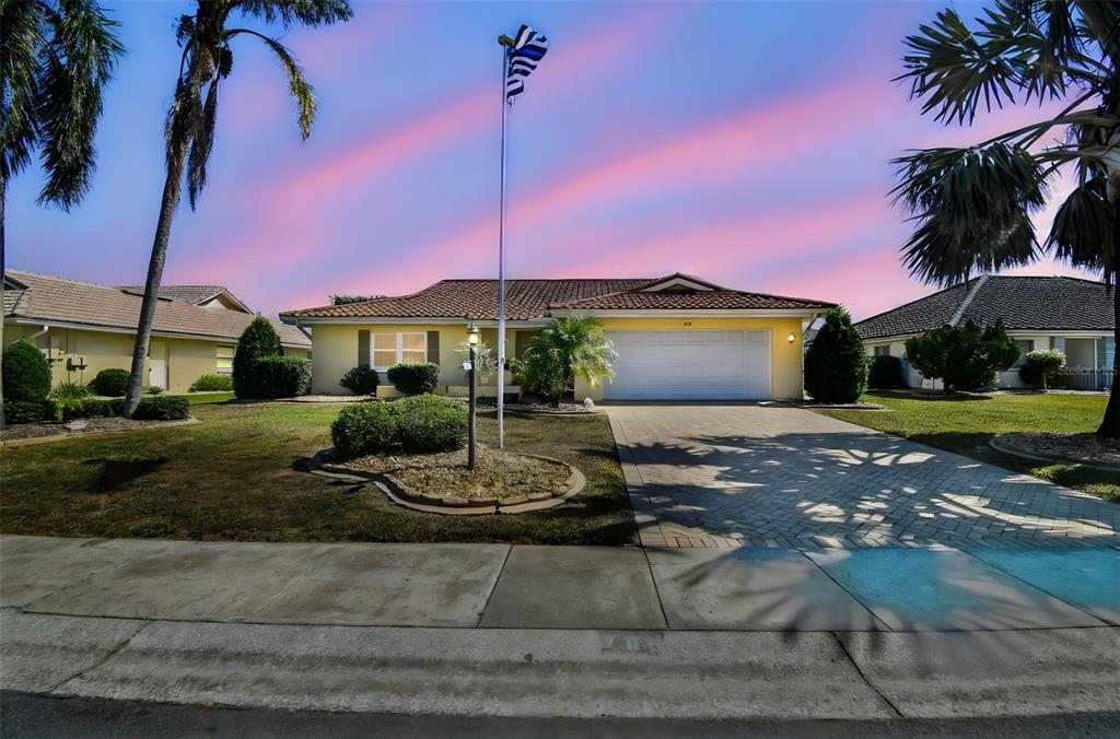 A single-story yellow house with a tiled roof and a paved driveway at sunset — 706 PLUMBROOK ROAD, SUN CITY CENTER, FL