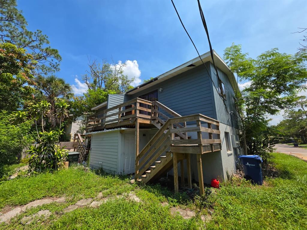 The exterior of a two-story house features a wooden deck with stairs and overgrown landscaping — 7087 BRENTFORD ROAD, SARASOTA, FL