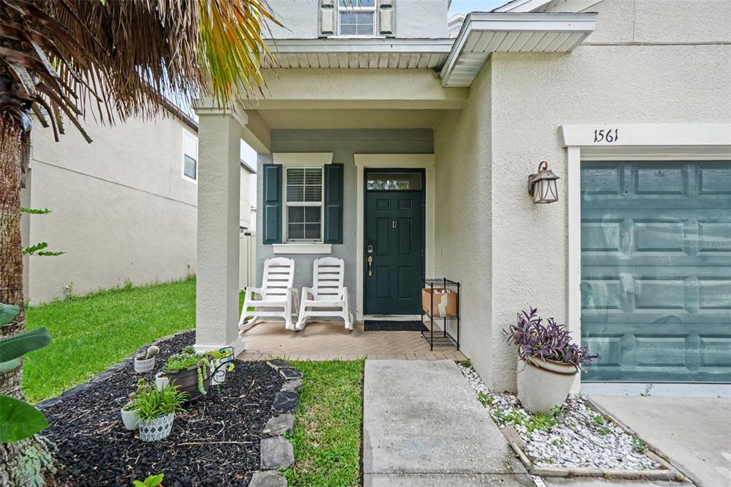 The exterior of a house features a covered porch, a dark green door, and white rockers — 1561 TALLULAH TERRACE, WESLEY CHAPEL, FL