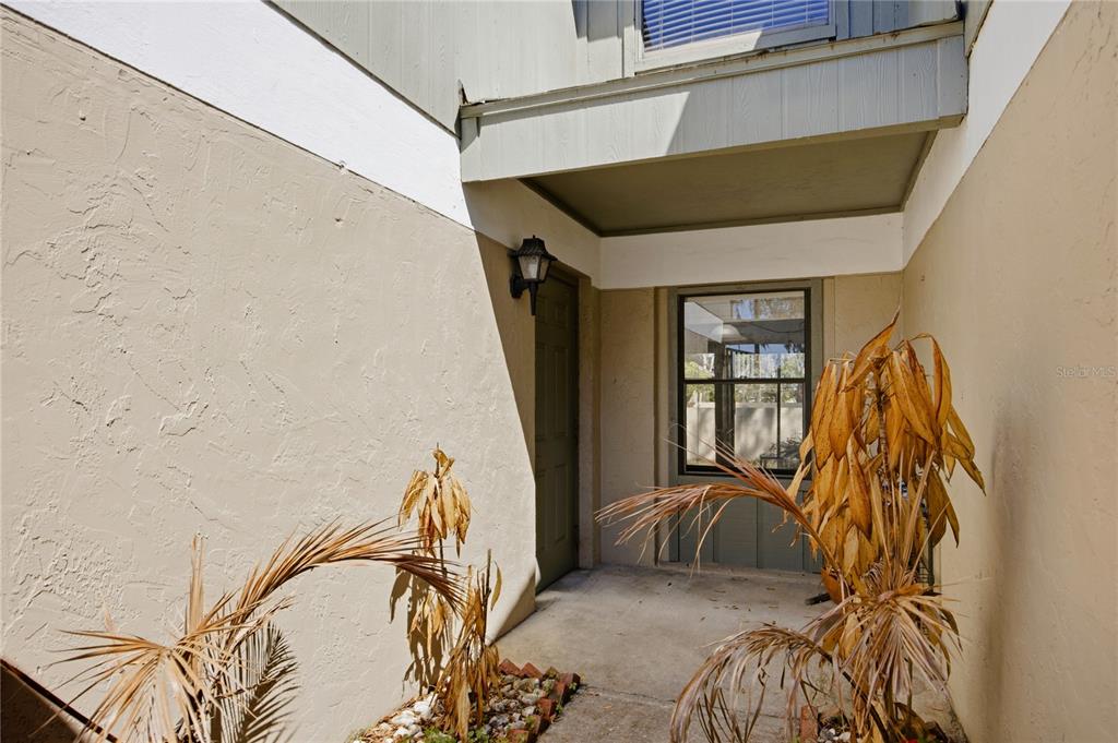 A covered entryway features a beige stucco wall, a dark door, and a window — 7200 SW 8TH AVENUE UNIT S119, GAINESVILLE, FL