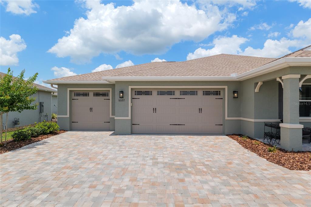 The exterior of a house features a three-car garage, a paved driveway, and light-colored siding — 9577 SW 82ND STREET ROAD, OCALA, FL