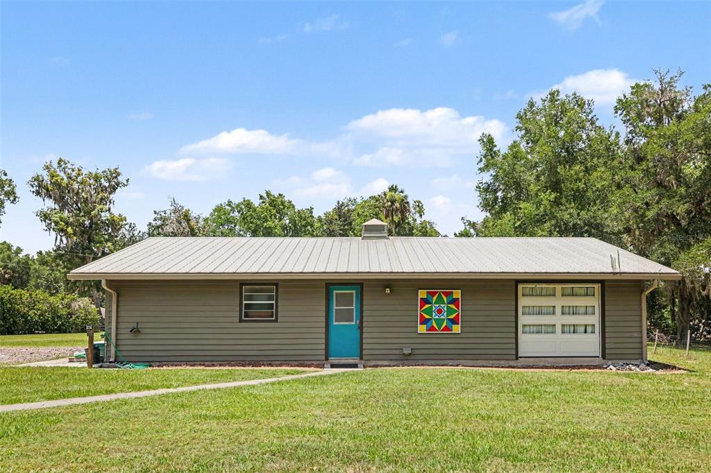 A single-story house with gray siding, a metal roof, a blue door, and a quilt square — 11165 E OWNBEY COURT, FLORAL CITY, FL