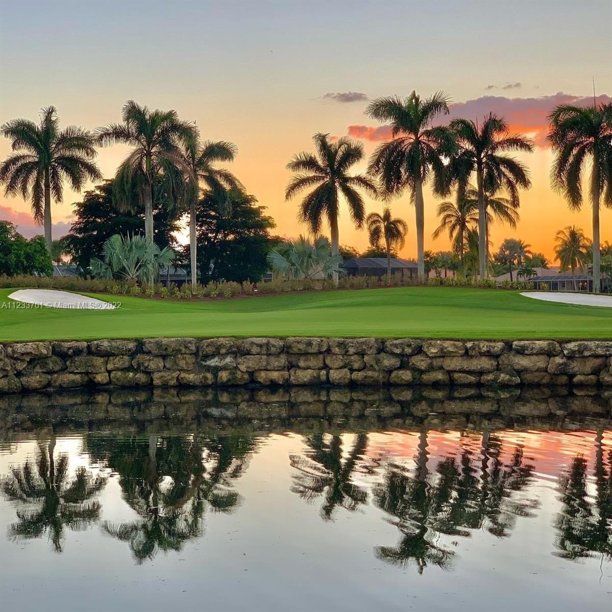 A golf course green sits behind a stone retaining wall and a reflective pond at sunset — 2054 Applegate Ave, Port Charlotte FL 33953, PORT CHARLOTTE, FL