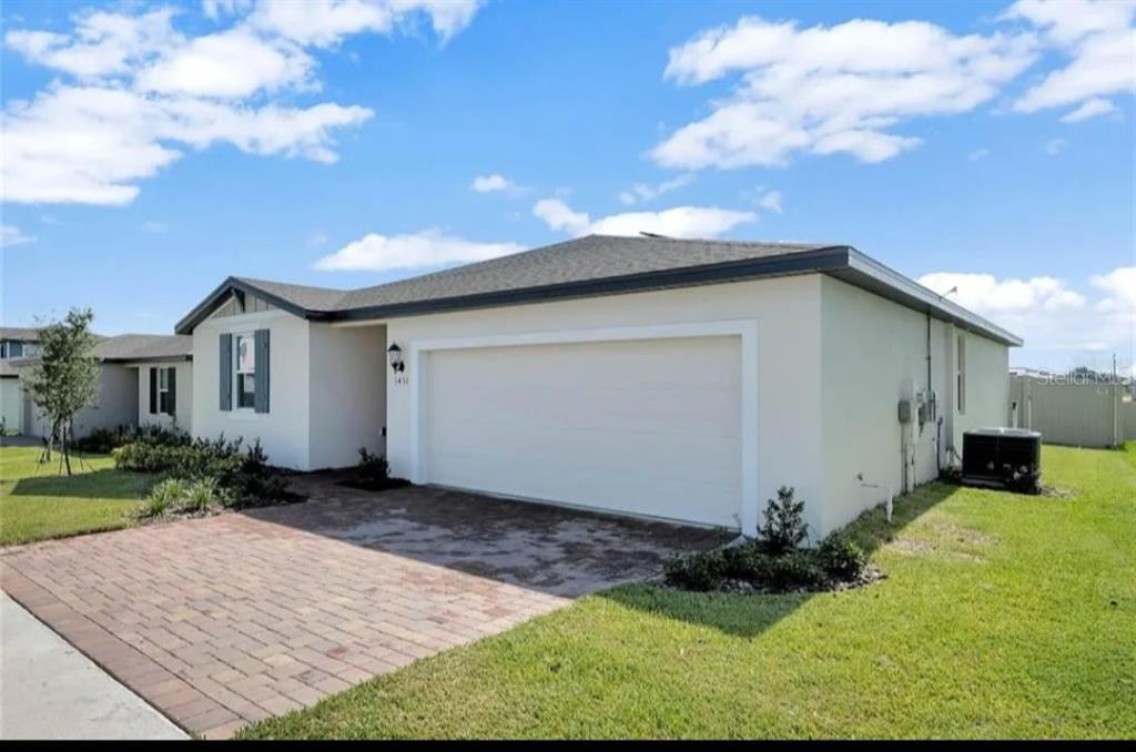 A single-story house with a white stucco exterior, a two-car garage, and a brick driveway — 1431 SAGUARO STREET, DAVENPORT, FL