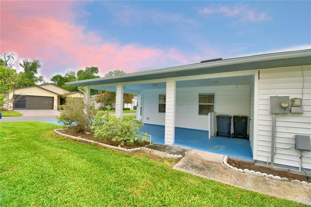 A covered patio with a blue floor and white siding sits beside a grassy lawn — 1690 COLONNADES CIRCLE N, LAKELAND, FL