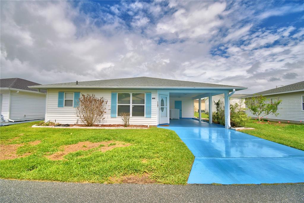 A single-story house with white siding, blue shutters, and a painted blue carport and driveway — 1690 COLONNADES CIRCLE N, LAKELAND, FL