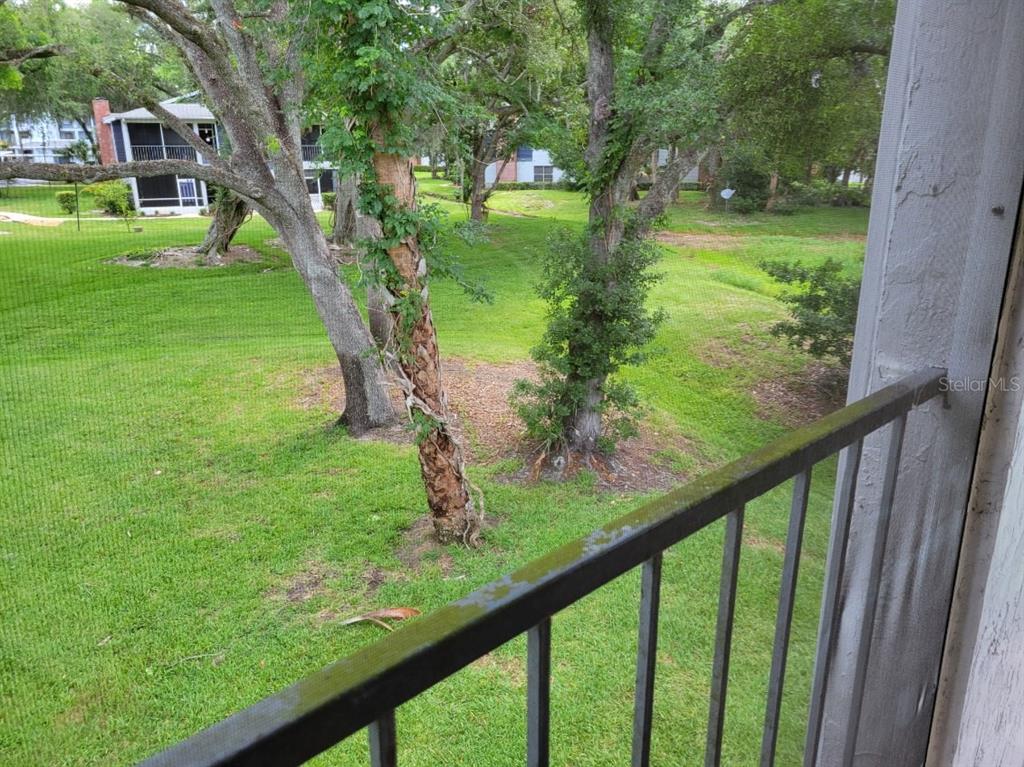 A view from a screened-in balcony overlooking a grassy yard with trees and nearby buildings — 1808 NORTHLAKE DRIVE UNIT 1808, SANFORD, FL