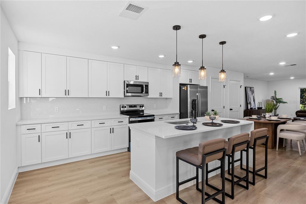 A modern kitchen features white cabinetry, a central island with bar seating, and light flooring — 711 CLEMSON DRIVE, ALTAMONTE SPRINGS, FL
