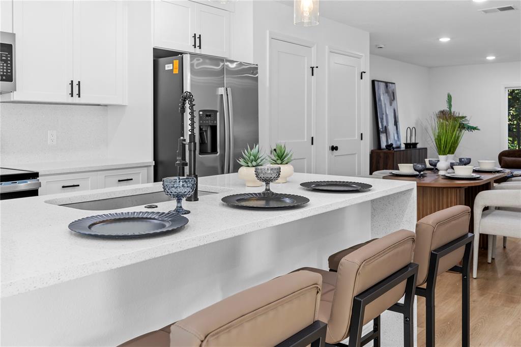 A modern kitchen features a white quartz island, stainless steel appliances, and light wood flooring — 711 CLEMSON DRIVE, ALTAMONTE SPRINGS, FL