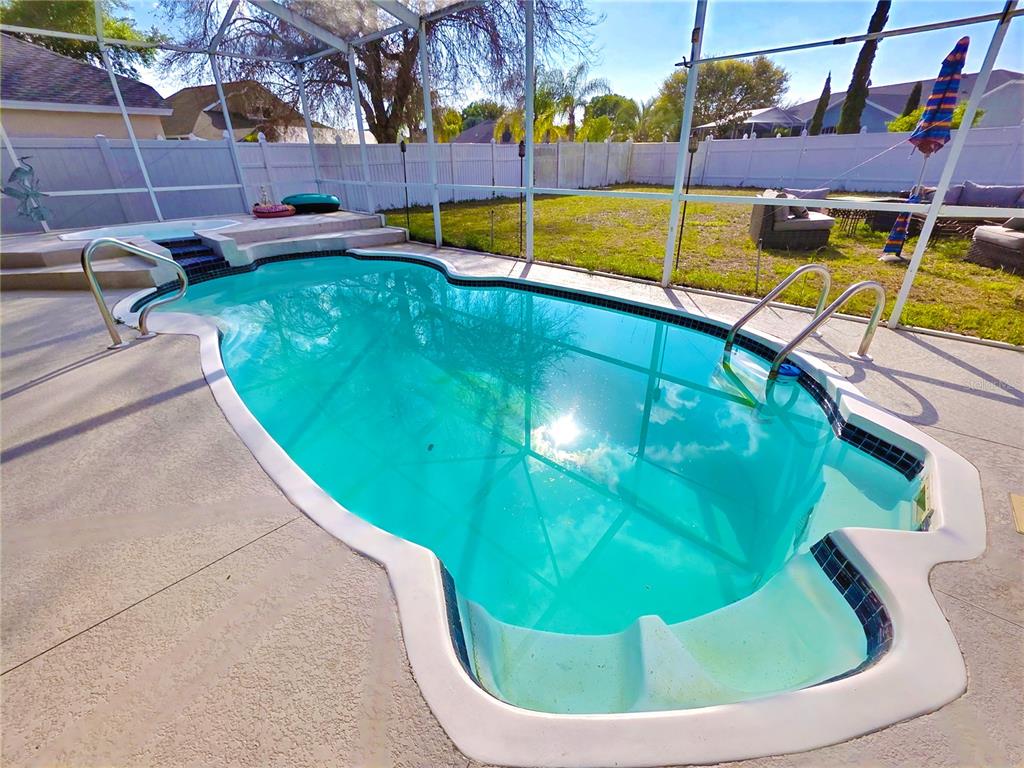A swimming pool and attached hot tub are enclosed within a screened-in patio area — 7927 ROUNDELAY DRIVE, NEW PORT RICHEY, FL