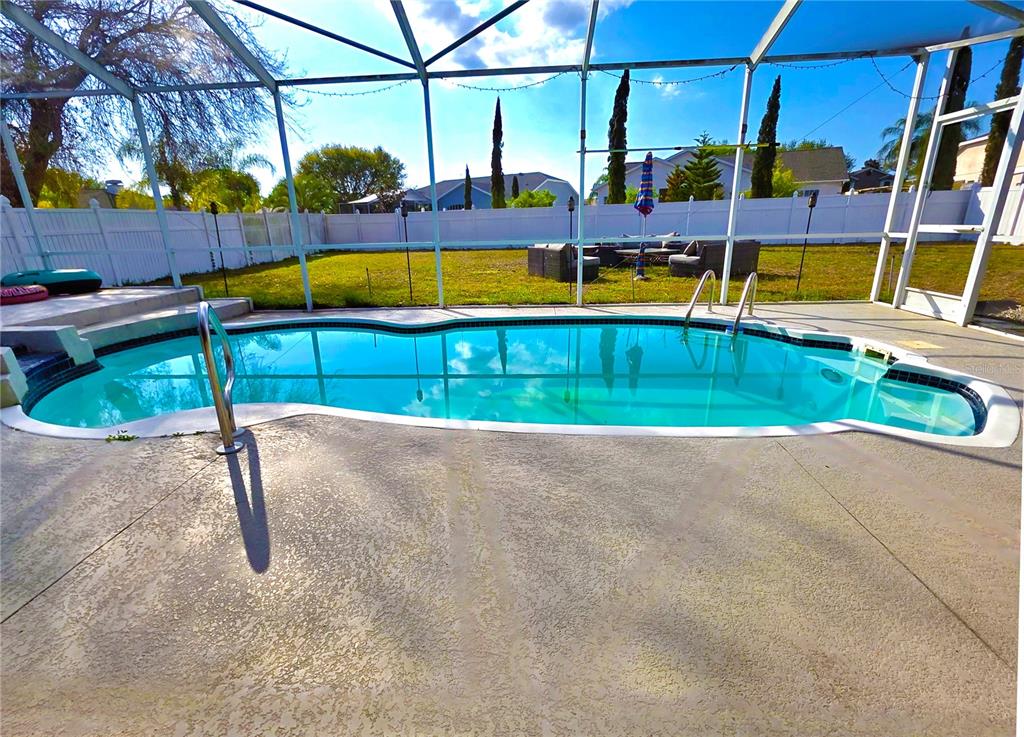 A screened-in swimming pool sits on a concrete patio in a fenced backyard — 7927 ROUNDELAY DRIVE, NEW PORT RICHEY, FL