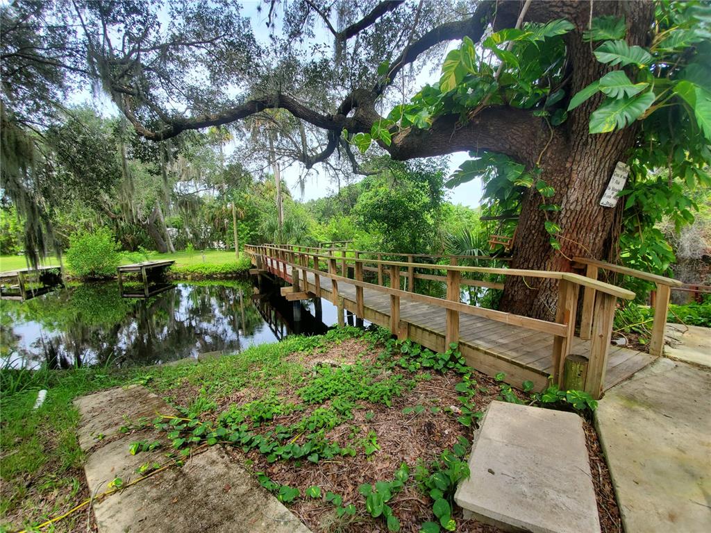 A wooden footbridge crosses a small pond beneath a large tree with hanging moss — 29208 SNOOK CIRCLE, PUNTA GORDA, FL