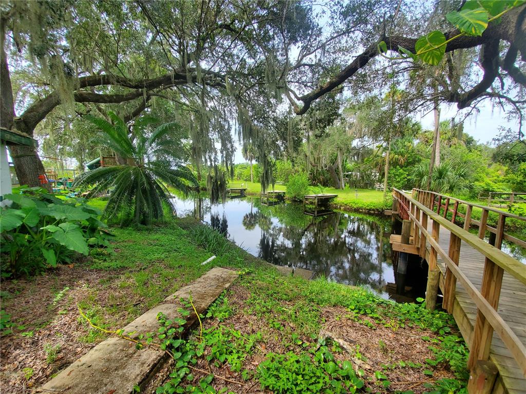 A wooden footbridge spans a narrow canal surrounded by lush trees and vegetation — 29208 SNOOK CIRCLE, PUNTA GORDA, FL