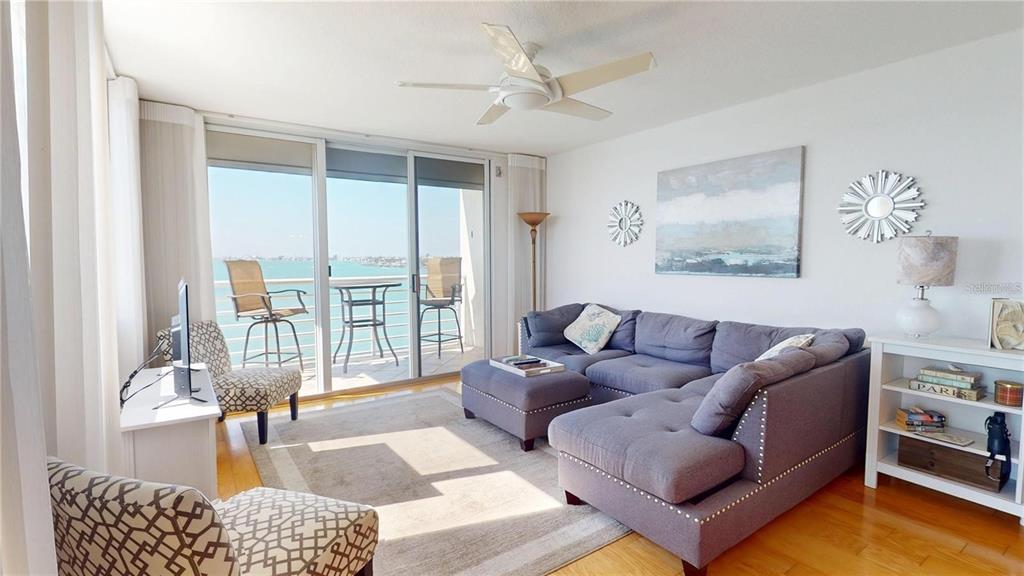 A living room features a gray sectional sofa, a balcony with water views, and hardwood floors — 6105 BAHIA DEL MAR CIRCLE UNIT 682, ST PETERSBURG, FL