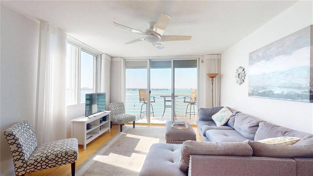 A living room with a gray sectional, patterned chairs, and a balcony overlooking the water — 6105 BAHIA DEL MAR CIRCLE UNIT 682, ST PETERSBURG, FL
