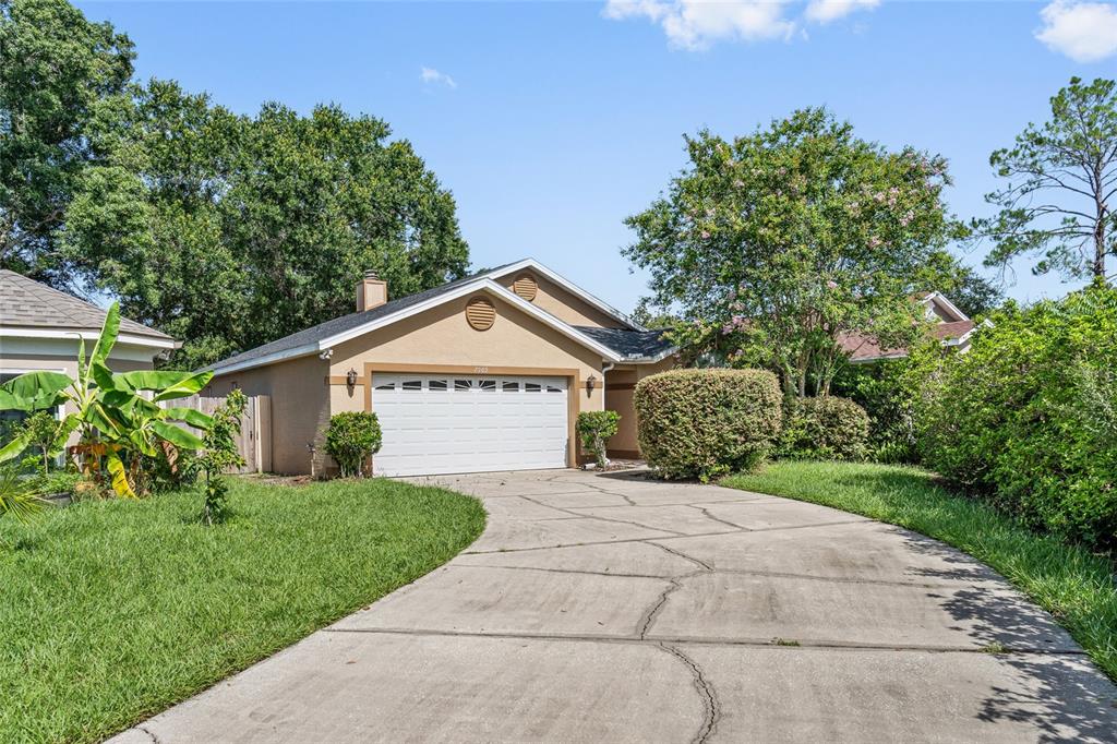 A tan single-story house features a two-car garage, a cracked concrete driveway, and mature landscaping — 7909 WALDORF COURT, ORLANDO, FL
