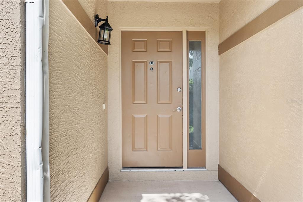 A tan front door with a side window is set in a stucco entryway — 7909 WALDORF COURT, ORLANDO, FL