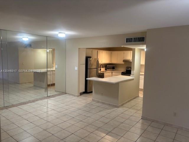A kitchen with light-colored cabinets and tile flooring opens into a tiled living area — 9002 SW 137 ST # 27, Miami FL 33176, MIAMI, FL
