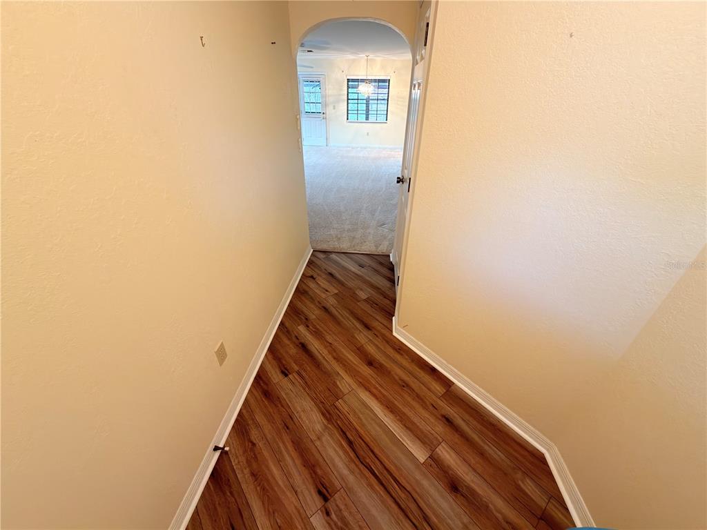 A hallway with wood-look flooring leads through an arched doorway into a carpeted room — 1241 SHAMROCK DRIVE, SEBRING, FL