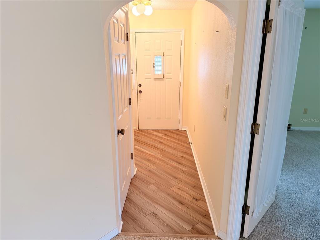 A hallway with wood-look flooring leads to a white front door under an arched entryway — 1241 SHAMROCK DRIVE, SEBRING, FL