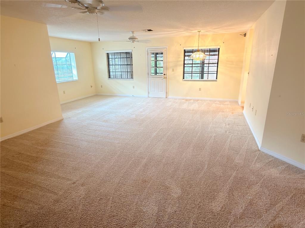 A spacious, carpeted living area features light yellow walls, ceiling fans, and multiple windows — 1241 SHAMROCK DRIVE, SEBRING, FL
