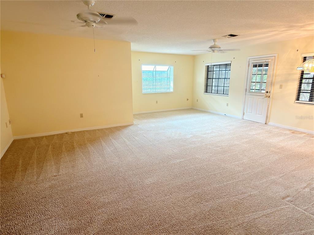 A spacious room with beige carpeting, light yellow walls, two ceiling fans, and a door — 1241 SHAMROCK DRIVE, SEBRING, FL