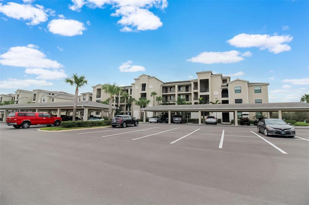 An exterior view of a multi-story apartment building with covered parking and a paved lot — 17810 GAWTHROP DRIVE UNIT 207, BRADENTON, FL