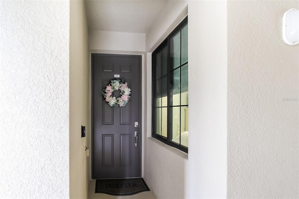 A dark gray front door with a floral wreath and a window sits in an entryway — 17810 GAWTHROP DRIVE UNIT 207, BRADENTON, FL