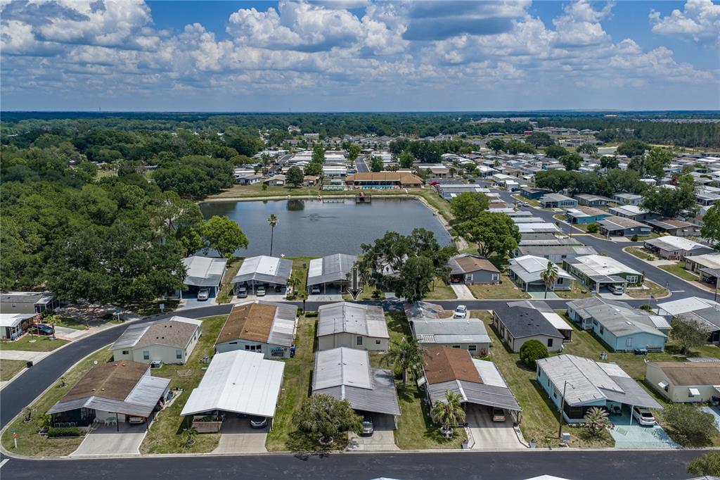 An aerial view shows a manufactured home community with a central pond and surrounding houses — 3201 HIDDEN LAKE DRIVE, WESLEY CHAPEL, FL