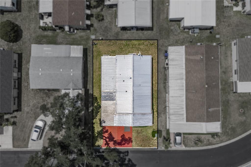 An aerial view shows a rectangular house with a metal roof and a red patio — 3201 HIDDEN LAKE DRIVE, WESLEY CHAPEL, FL
