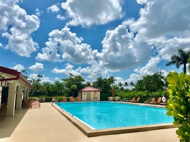 A rectangular swimming pool sits on a patio next to a small building under clouds — 3250 SOUTHSHORE DRIVE UNIT 53B, PUNTA GORDA, FL