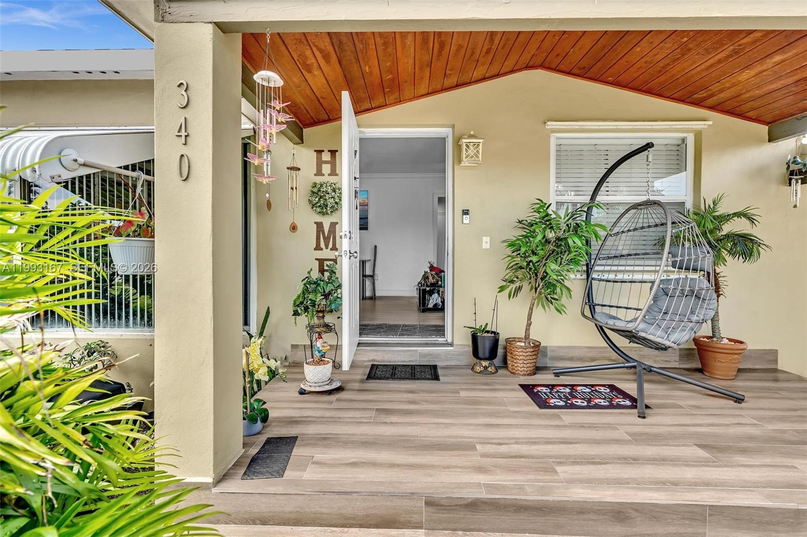 A covered front porch features wood-look tile flooring, a hanging chair, and an open door — 340 W 55th St, Hialeah FL 33012, HIALEAH, FL